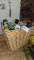 Photo of various Rust-Oleum spray cans and bottles arranged in a wicker basket and on the floor, showing labels such as Flex Seal, Farm & Implement, Stop Rust, Metallic finishes, and clear protective enamel.