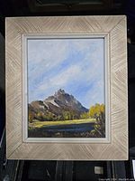 Full view of the framed oil painting showing a mountain landscape with blue sky and yellow-green trees