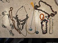 Photo showing 13 assorted jewelry items laid out on surface with various necklaces and bracelets.