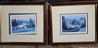 Two framed prints showing rural spring garden scenes with cottages, trees, and rivers under soft lighting. Frames are wood with gold and red finish and off-white matting.
