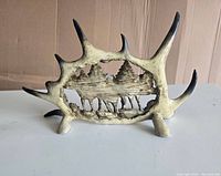 Side view of antler carving showing forest scene with trees and detailed ground, natural antler texture and points visible.