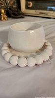 Photo showing white ceramic round jewelry holder on a base made of large white wooden beads, highlighting the shape and texture of the holder.