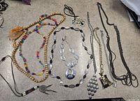Photo of assorted jewelry necklaces and pendants laid on a flat surface showing colorful beads, wooden beads, stone beads, silver and gold tone chains with various pendants