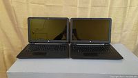 Front view of two HP 15 Series 15 inch laptops side by side with screens open and keyboards visible