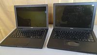 Pair of black Apple MacBooks open showing keyboards and displays off.