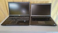 Two Dell Vostro laptops side by side on a grey surface under warm lighting; left laptop is larger with numeric keypad, right laptop is smaller without numeric keypad.