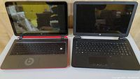 Two 15 inch HP 15 series laptops side by side, one black with red base and Beats logo on palm rest, other all black, screens off and reflect surroundings.