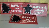 Three red Christmas countdown signs with blackboards shaped as a Christmas tree and a star, displayed together on a surface.
