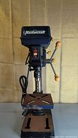 Front view of Mastercraft drill press showing power switch, drill chuck, base, and control handles.