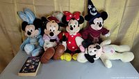 Full view of all five Disney plush toys featuring Mickey and Minnie in various costumes, plus Disney trivia book on table
