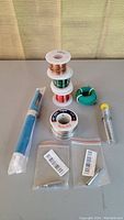 Lot contents showing blue solder sucker, wire rolls in several colors, solder rolls, and soldering tips in plastic bags.