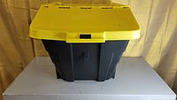 Side view of a black plastic storage bin with a closed yellow lid.