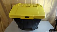 Front view of closed black stackable storage bin with yellow lid and clip