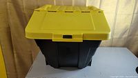Front view of black storage bin with closed yellow lid highlighting lid clip and hinged design.