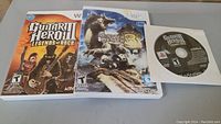 Three Wii game discs shown with cases and cover art: Guitar Hero III Legends of Rock (in case and loose disc) and Monster Hunter Tri (in case)