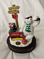 Front and side view of the Coca-Cola music box figurine including the polar bear, small black bear, Coca-Cola cooler, and directional post.