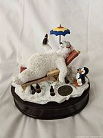 Front view of Coca-Cola Heritage Collection music box with polar bear lying on lounge chair holding Coke bottle, penguin figure, and umbrella on snow base.