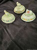 Three Lenox porcelain decorative eggs with animal figurine lids photographed on black fabric.