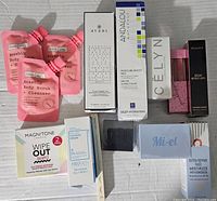 All beauty items arranged on white cloth with brand and product names visible; assortment includes body care, skincare, and makeup products.