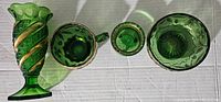 Top view of five emerald green pressed glass items showing gold accents and embossed patterns.
