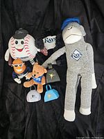 Various Tampa Bay Rays stadium giveaway plush toys including a baseball character, gorilla, monkey, tiger, and teddy bear, plus three souvenir bells with Rays logo.
