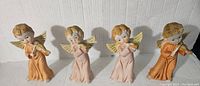 Four vintage Homco angel figurines displayed in a row, each in a different musical pose and wearing peach or apricot colored robes.