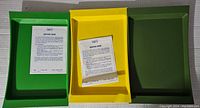 Three rectangular serving trays in green, yellow, and dark green with original care instructions placed on them, showing color, shape, and size.