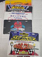 Stack of Old Town Saturday Nite Cruise license plates showing various editions and anniversary plates with colorful automotive-themed designs.