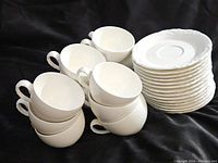 12 white porcelain cups stacked next to matching saucers, showing quantity and design