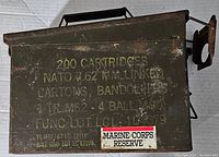 Front and top view of vintage metal ammo box showing stencil markings and Marine Corps Reserve sticker.