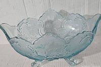 Blue translucent Jeanette glass footed fruit bowl with ornate pressed floral and leaf pattern, scalloped edges, and three detailed feet.