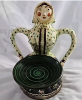 Front view of the vintage Kantor Karcagi clay figurine with distinctive facial features and arms forming handles around a green spiral patterned tray.