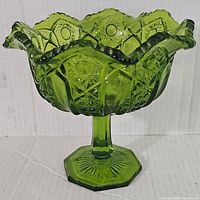 Side view of the green glass compote showing ruffled edge, intricate pressed designs, and hexagonal pedestal base.