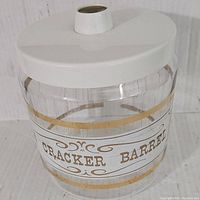 Full view of vintage clear glass Pyrex canister with white lid and Cracker Barrel gold label