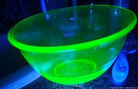 Uranium glass bowl glowing bright green under UV light showing its characteristic glow.