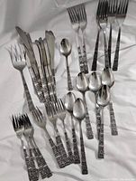 Full top view of flatware set laid out showing spoons and forks with detailed patterned handles.