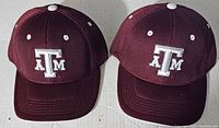 Two maroon Texas A&M baseball caps with white embroidered logos, shown from front top angle.