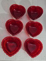 Six ruby red heart-shaped glass bowls arranged in two rows of three on a white surface