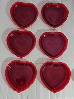 Set of six ruby red heart-shaped glass dishes arranged in two rows of three on a white background.