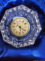 Octagonal Waterford crystal clock with clear, faceted edges and a round clock face that includes Roman numerals, black hands, and a gold-tone bezel.