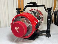 Front side view of the red and clear cylindrical Ikelite digital camera underwater housing with black handle, showing the branded red front cover and tube.