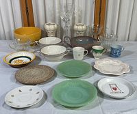 Full collection of vintage pottery, glass, and porcelain items arranged on white cloth, includes bowls, plates, cups, and glasses.