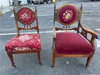 Front and side view of two vintage wooden chairs with red fabric upholstery, showing detailed floral tapestry on backrests and general aged condition.