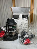 Wayne 1/3 Hp stainless steel submersible sump pump shown with box and accessories in plastic bag.
