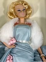 Close-up of Barbie doll's upper body showing blonde hair, makeup, blue satin dress with pink flowers, and white fur stole