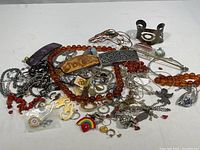 Photo showing assorted jewelry including beads, pins, rings, chains, a purple marbled barrette, and a silver-tone cuff bracelet.