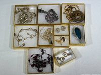 All costume jewelry items sorted in gold gift boxes, showing necklaces, pendants, and earrings.