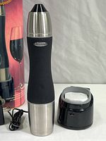 Main wine saver device, black and stainless steel, next to black storage base and power supply cord.