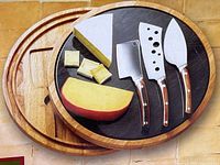 Four pieces of cheese knives with wooden handles laid out on a round marble cutting board on wood base with sample cheese wedges.