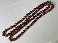Full view of the polished stone bead necklace laid out in a circular shape on a light cloth surface showing varied shades of brown beads.